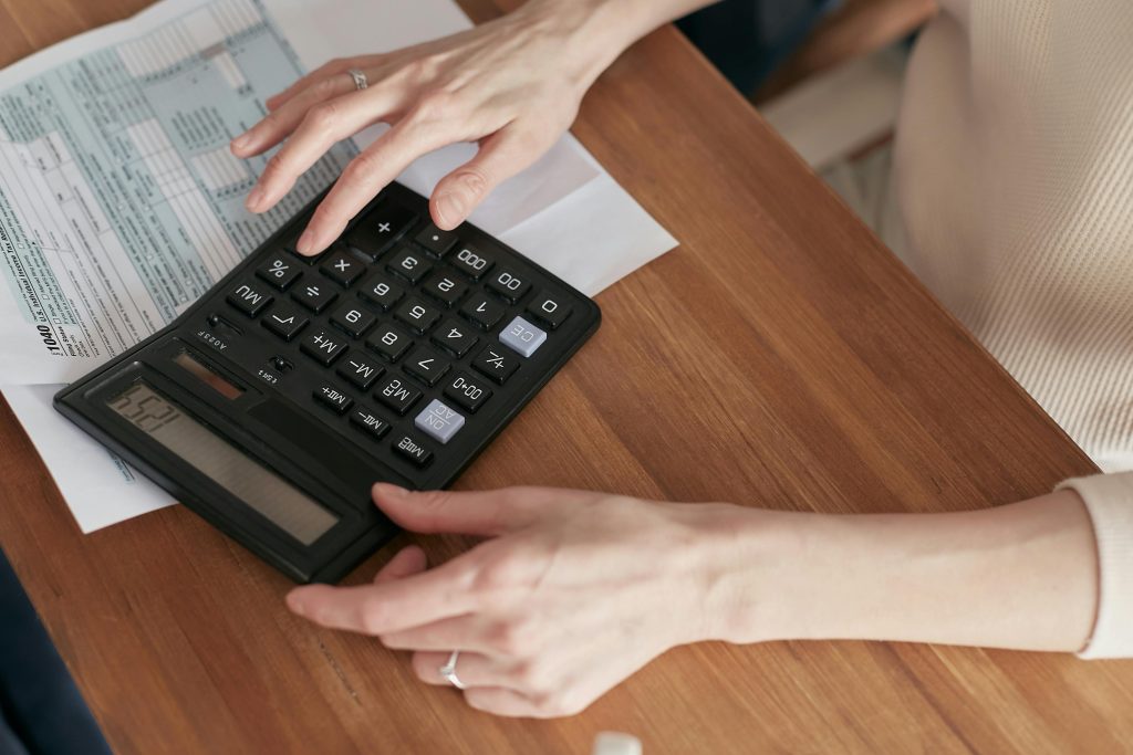 Hand using calculator to review financial documents for real estate invoice generation